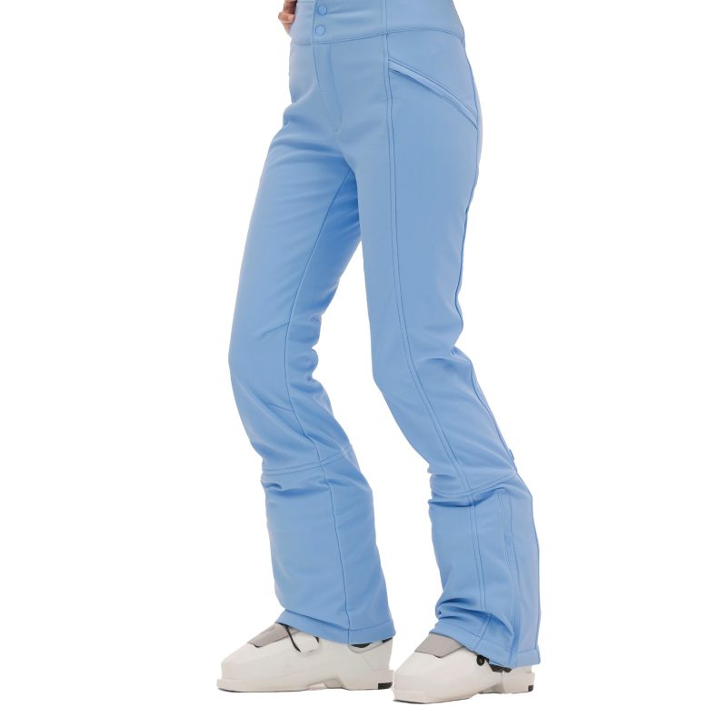 A person dressed in Halfdays Emma Pant ski pants and white ski boots stands on a pristine white background.