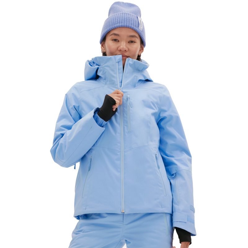 A woman in a light blue Halfdays Lawrence Jacket and matching pants, with a light blue beanie, is partially zipping up the jacket.